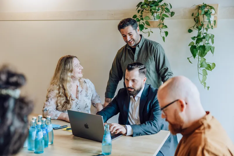 A group of four people having a meeting around a table with laptops and water bottles, with plants on the wall.
